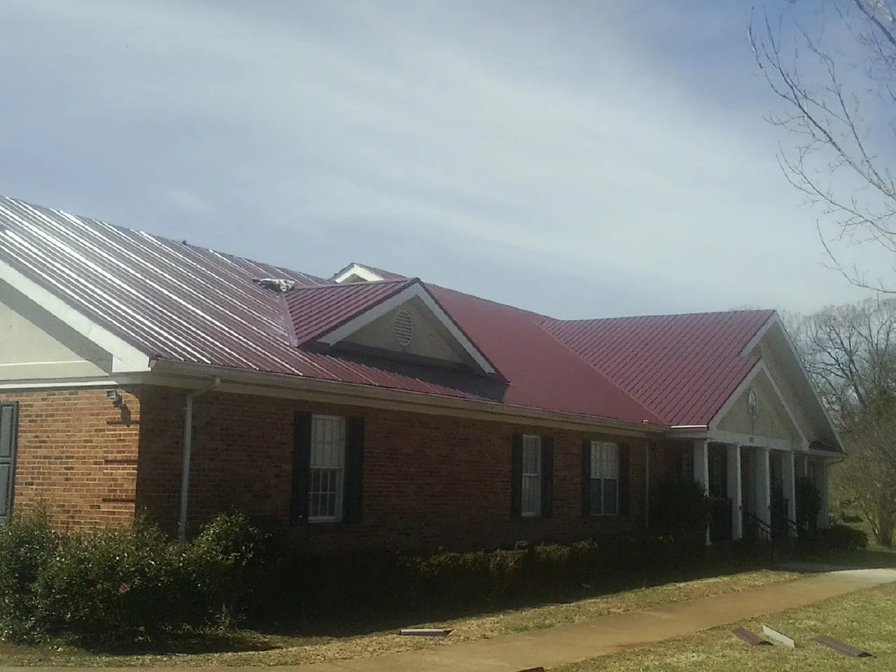 Red metal roof with gabled entries on a long brick building, from a Hail Damage Roof Repair job in Magalia