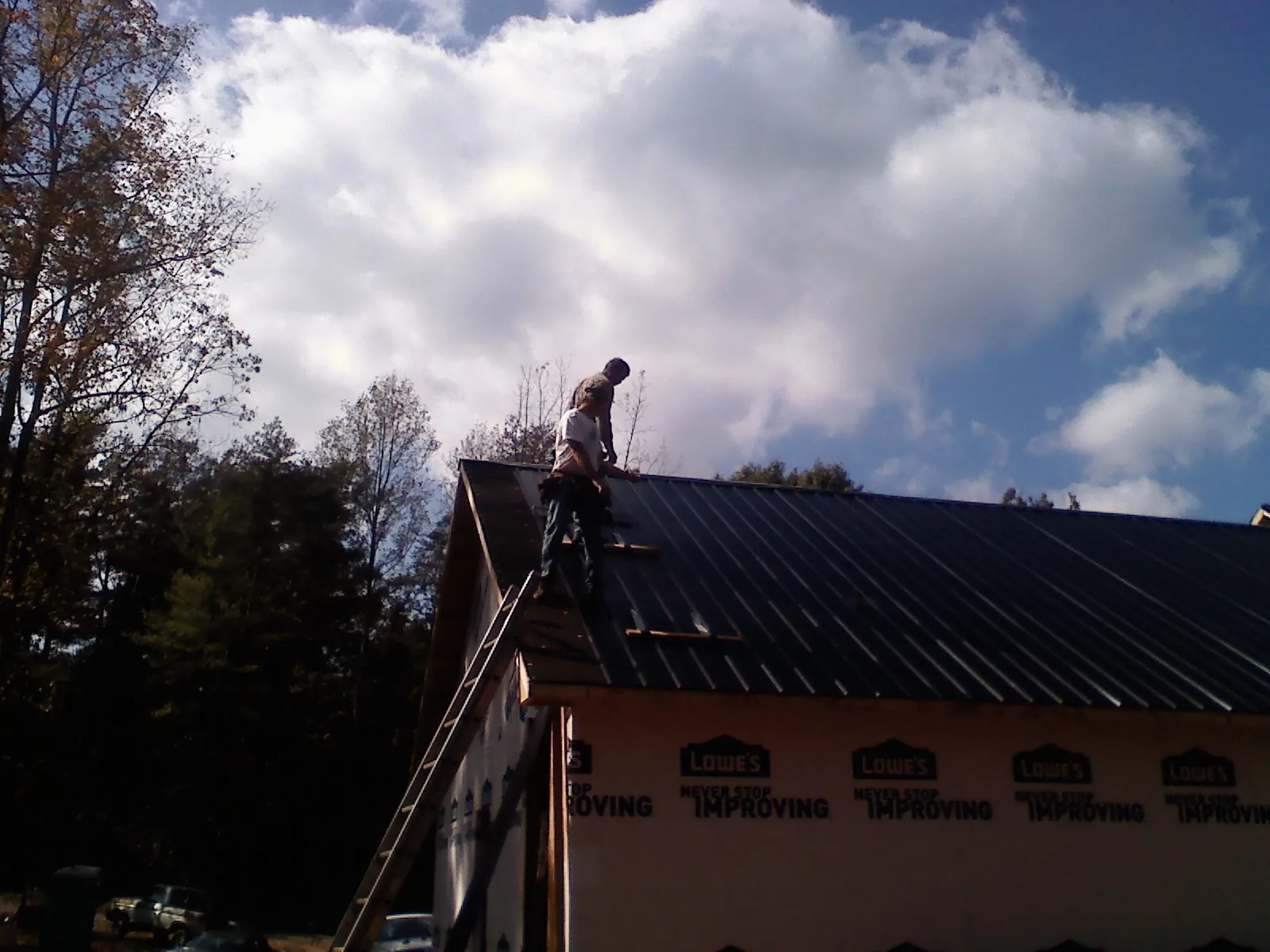 Roofer fastening dark metal panels high against a cloudy sky, from a Roof Inspection job in Magalia